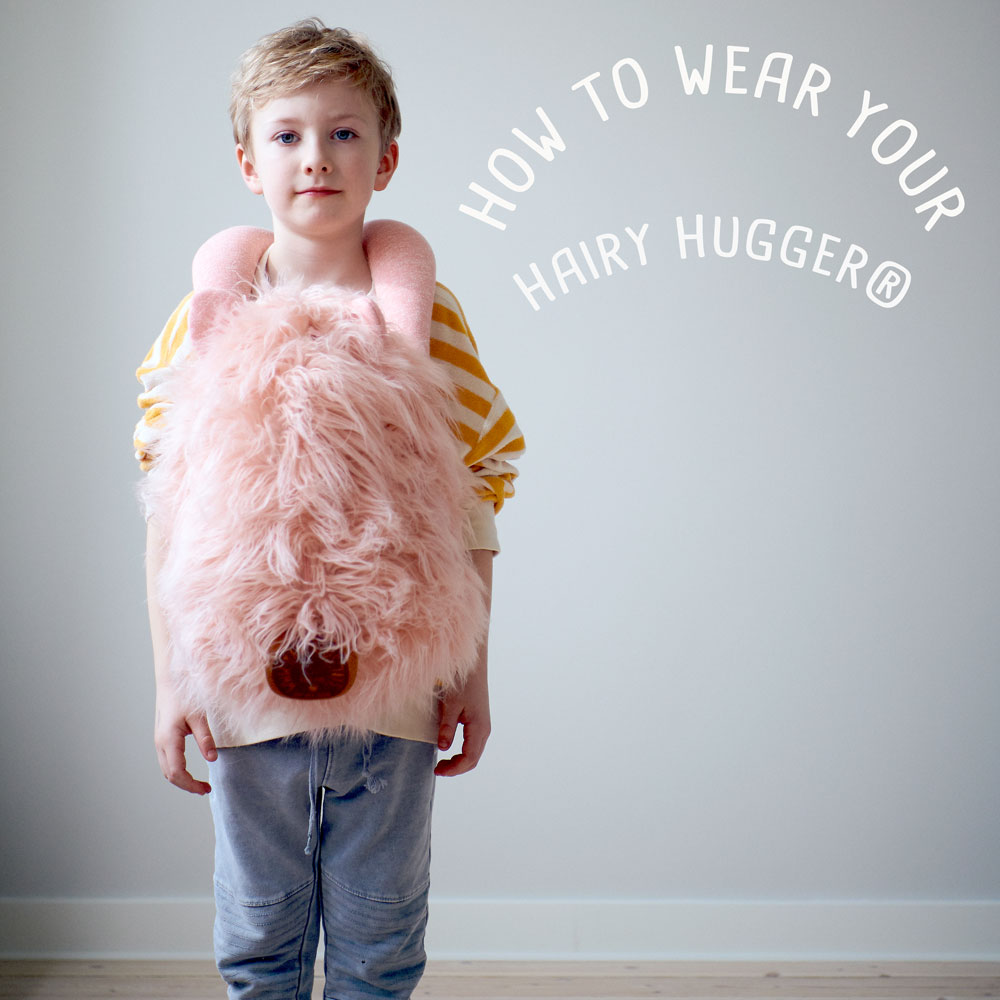 Hairy Hugger i lyserød sidder på maven af et barn